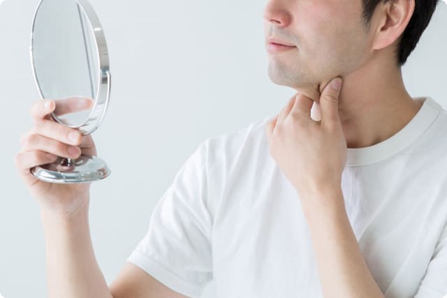 鏡を見ながら喉まわりの状態を確認する男性 - 銀座リリース整体院